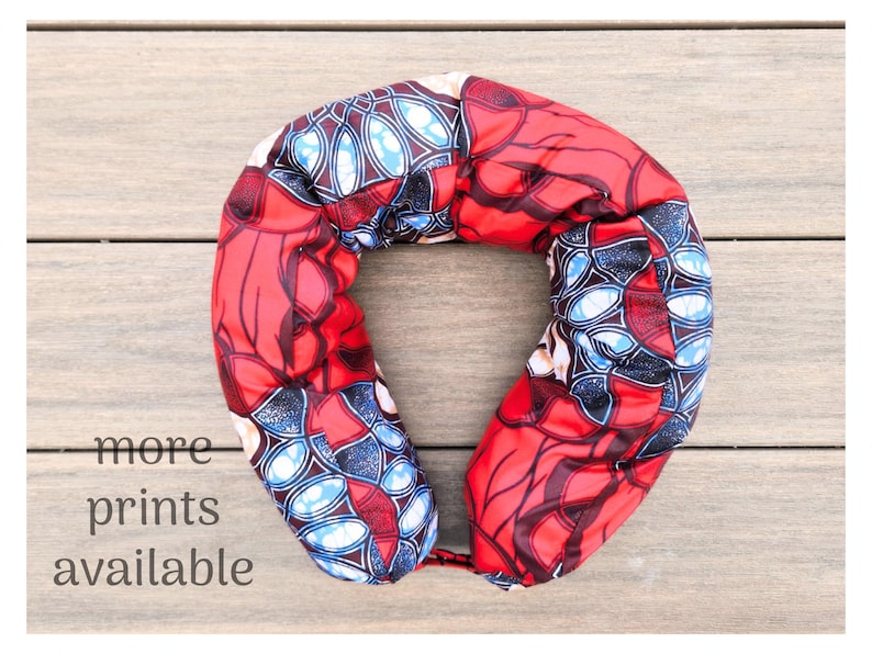 May include: A red and blue patterned travel neck pillow. The pillow has a U-shape design and is made of a soft, patterned fabric. The text "more prints available" is visible in the image.