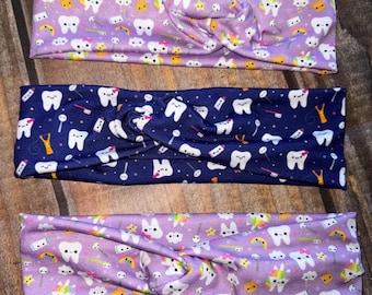 May include: Three colorful headbands with a pattern of cartoon teeth, toothbrushes, rainbows, stars, and unicorns. The headbands are made of a soft, stretchy fabric and are perfect for adding a fun and playful touch to any outfit.