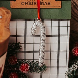 May include: A silver candy cane ornament with a red ribbon hanging from a gift box with a black and white plaid pattern. The gift box has a brown tag that says "Merry Christmas".