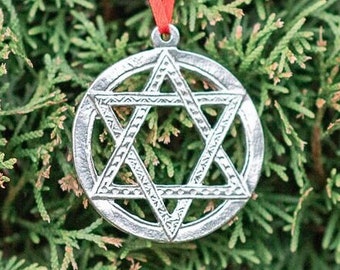 May include: A silver Star of David ornament with a red ribbon hanging on a green evergreen tree.