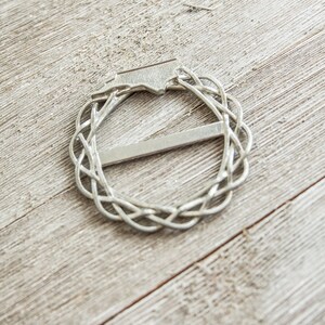 May include: A silver metal belt buckle with a Celtic knot design.