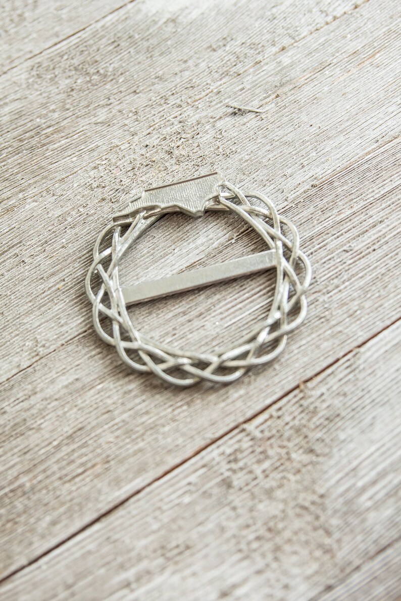 May include: A silver metal belt buckle with a Celtic knot design.