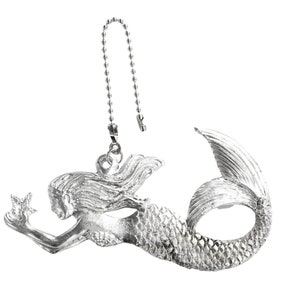 Puede incluir: Figura de sirena de plata con una cadena para colgar. La sirena sostiene una estrella en su mano y tiene una cola detallada.