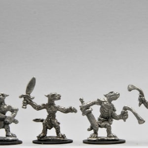 May include: Five miniature metal figurines of humanoid creatures with animalistic features, each holding a different weapon. The figures are painted in a silver color and stand on black bases.