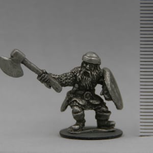 May include: A pewter miniature figurine of a dwarf warrior holding an axe and a shield. The dwarf is wearing chainmail armor and a helmet. The figurine is about 2 inches tall.