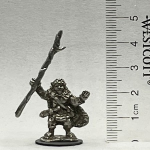May include: A miniature metal figurine of a goblin holding a staff. The goblin is wearing a fur-lined cloak and has a mischievous expression on its face.
