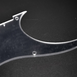 May include: A clear plastic guitar pickguard with two round holes. The pickguard is designed to fit a guitar.