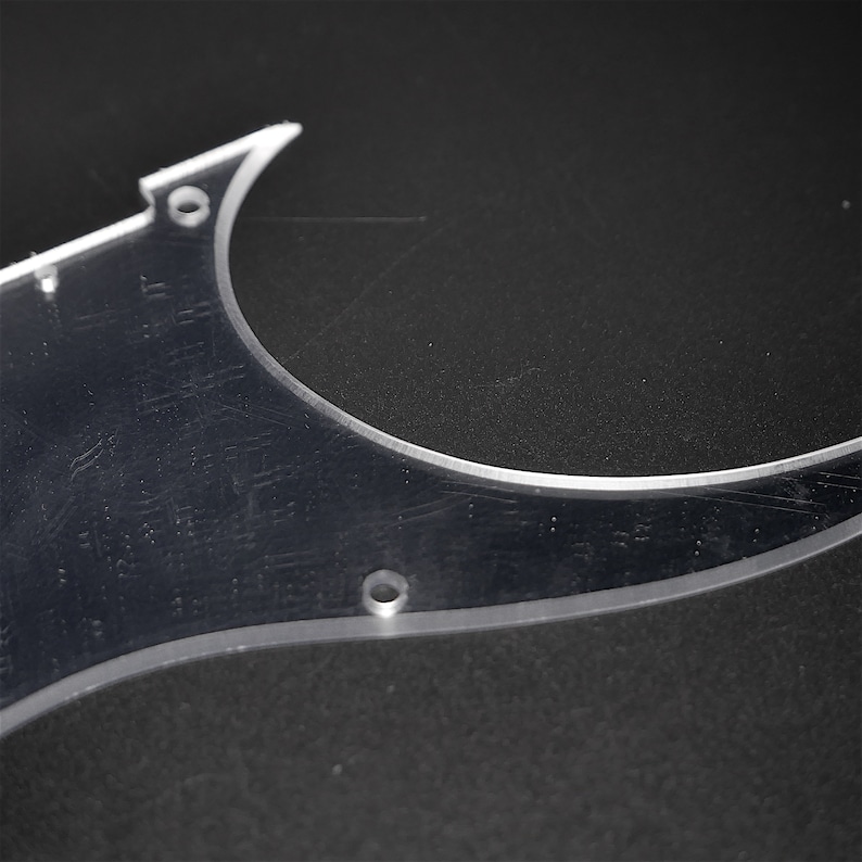 May include: A clear plastic guitar pickguard with two round holes. The pickguard is designed to fit a guitar.