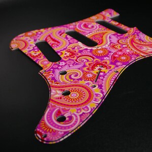 Peut inclure: Un pickguard de guitare à motif paisley rose et jaune. Le pickguard a une forme de guitare classique avec des découpes pour les micros et les commandes.