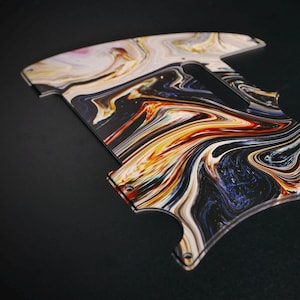 Peut inclure: Une plaque de protection pour guitare arborant un motif marbré tourbillonnant dans des tons de noir, blanc, orange et bleu profond. Ce composant plat en plastique profilé présente des ouvertures prédécoupées pour les micros et des trous.