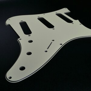 Peut inclure: Un pickguard de guitare blanc avec trois cavités de micros et plusieurs trous de vis.