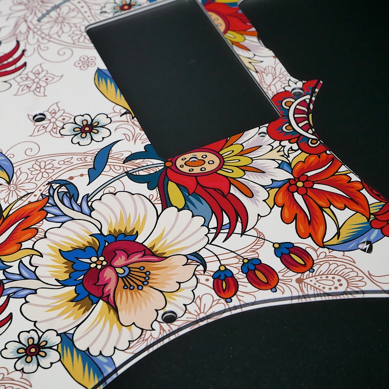 Puede incluir: Una placa de protecci&oacute;n de guitarra blanca con un patr&oacute;n floral colorido. El patr&oacute;n presenta flores rojas, amarillas, azules y verdes sobre un fondo blanco.