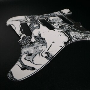 Peut inclure: Plaque de protection de guitare marbrée noir et blanc. La plaque de protection est en plastique transparent avec un motif marbré noir et blanc. La plaque de protection est conçue pour s'adapter à une guitare électrique standard.