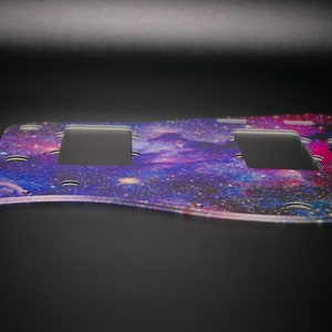 Op de afbeelding: Een paarse, blauwe en roze pickguard met een galaxy-thema met twee uitsparingen voor pickups.