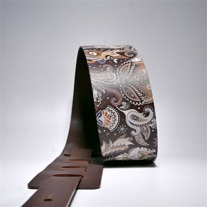 May include: A brown leather guitar strap with a paisley pattern in shades of brown, white, and orange.