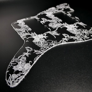May include: Black guitar pickguard with a white floral design.