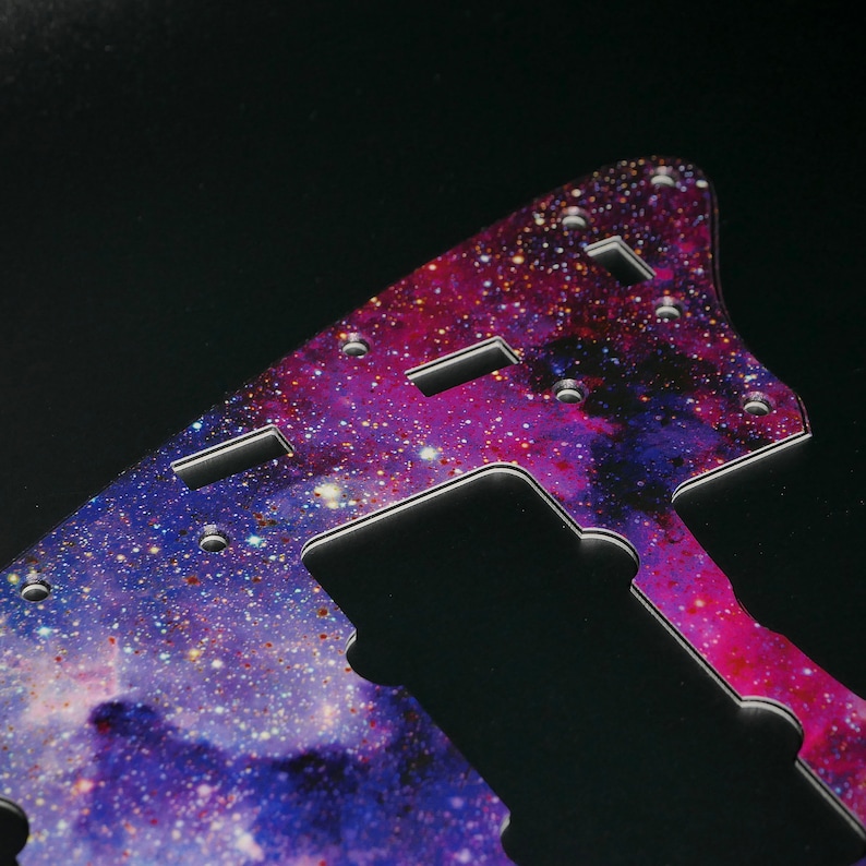 Op de afbeelding: Een gitaar pickguard met een galaxy print in tinten van paars, roze en blauw met gouden glitter accenten.