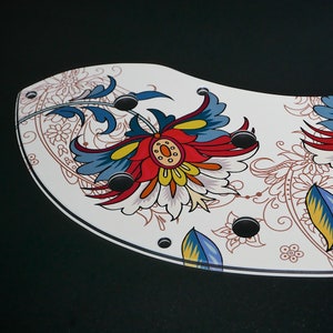 Puede incluir: Plato de cer&aacute;mica blanco con un dise&ntilde;o floral colorido. El dise&ntilde;o presenta flores rojas, azules, amarillas y blancas con detalles intrincados. El plato tiene un borde festoneado y un fondo negro.