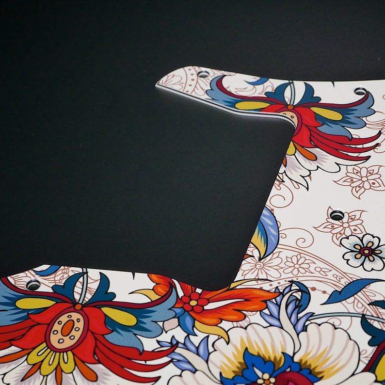 Puede incluir: Una placa de protecci&oacute;n de guitarra blanca con un patr&oacute;n floral en tonos rojos, azules, amarillos y blancos. La placa de protecci&oacute;n tiene un dise&ntilde;o paisley y est&aacute; hecha de un material duradero.