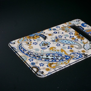 May include: A white guitar pickguard with a paisley pattern in shades of blue, gold, and black.