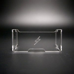 Op de afbeelding: Een heldere acryl kaarthouder met een bliksemschicht gegraveerd op de voorkant. De houder heeft een rechthoekige vorm met een gebogen bovenkant en een uitsparing aan de onderkant. De achtergrond is een zwart-grijze gradiënt.