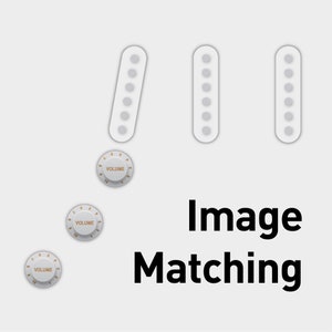 Puede incluir: Tres botones de guitarra blancos con un botón de volumen blanco con texto y números negros. El texto dice "VOLUME". Los botones están dispuestos en una fila con el botón de volumen en el centro.