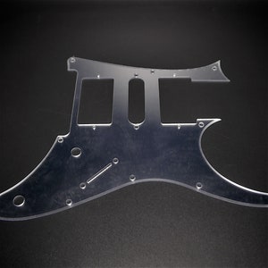 May include: A clear plastic guitar pickguard with multiple holes and cutouts for a guitar.