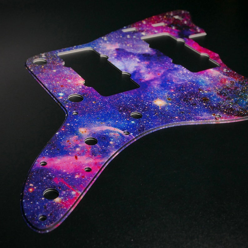 Op de afbeelding: Een paars en roze galaxy-thema gitaar pickguard met een sterrenhemel ontwerp. De pickguard heeft drie pick-up uitsparingen en een verscheidenheid aan schroefgaten.