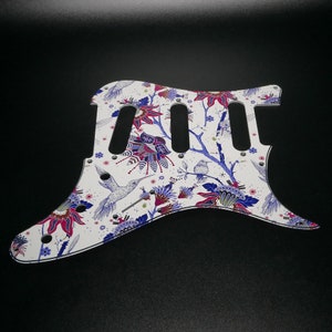 Pu&ograve; includere: Battuta per chitarra bianca con un design floreale e colibr&igrave; in tonalit&agrave; di blu, rosa e verde.