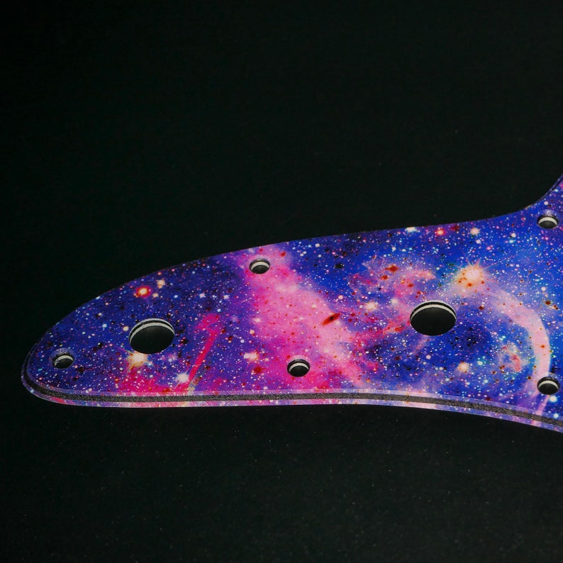 Op de afbeelding: Een paarse en roze pickguard met een galaxie-thema met meerdere gaten voor bevestigingsschroeven.