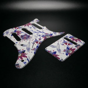 Pu&ograve; includere: Battuta per chitarra bianca con un motivo floreale che presenta colibr&igrave;, fiori e foglie in tonalit&agrave; di blu, viola e rosso.