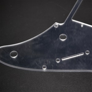 May include: Clear plastic guitar pickguard with multiple round holes and a single rectangular slot.