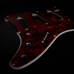 Peut inclure: Un pickguard en écaille de tortue pour une guitare électrique. Le pickguard a une bordure blanche et trois cavités de micros.