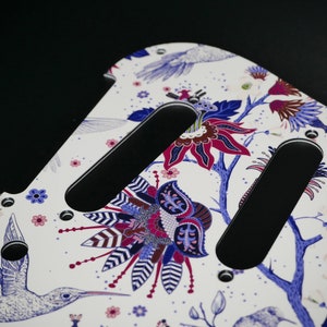 Pu&ograve; includere: Battuta di chitarra bianca con un motivo floreale in tonalit&agrave; di blu, rosa e viola. La battuta ha due cavit&agrave; per pickup nere.