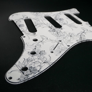 Peut inclure: Plaque de protection de guitare blanche avec un motif floral noir.