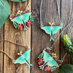 May include: Four necklaces featuring acrylic Luna moth pendants. Two pendants show a moth with green wings and red accents, while two show the moth alone. The pendants are attached to gold or silver-toned metal chains.