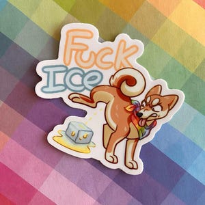 May include: A die-cut sticker featuring a cartoon Shiba Inu dog wearing a rainbow bandana, urinating on a single ice cube. The text "Fuck Ice" is written in orange and blue bubble letters above the dog. The sticker has a white border.