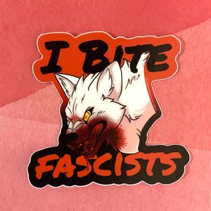May include: A sticker featuring a white wolf with yellow eyes and blood around its mouth. The text "I BITE FASCISTS" is in black and orange, with a red background.