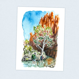 May include: Two people hike through a stream in a canyon. The canyon walls are red and the sky is blue. A green tree grows on the side of the canyon.