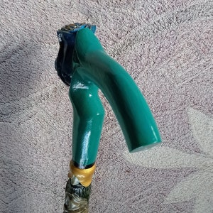 Puede incluir: Un bast&oacute;n de caminar verde azulado con un mango de madera tallado en forma de rosa. El mango est&aacute; pintado con detalles dorados y tiene una flor azul en la parte superior.