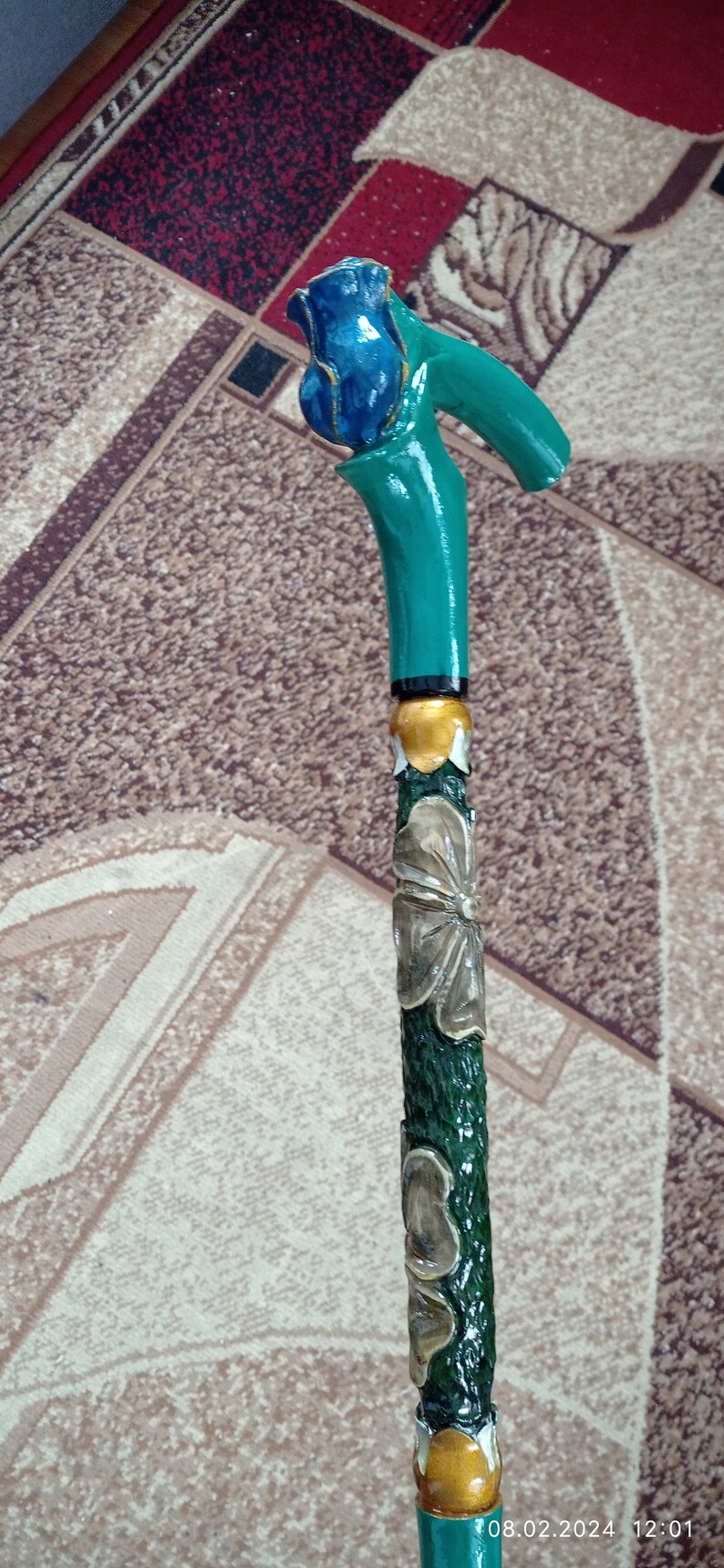Puede incluir: Un bast&oacute;n de madera con un mango pintado de verde y azul con forma de rosa. El bast&oacute;n est&aacute; decorado con flores talladas y detalles dorados.