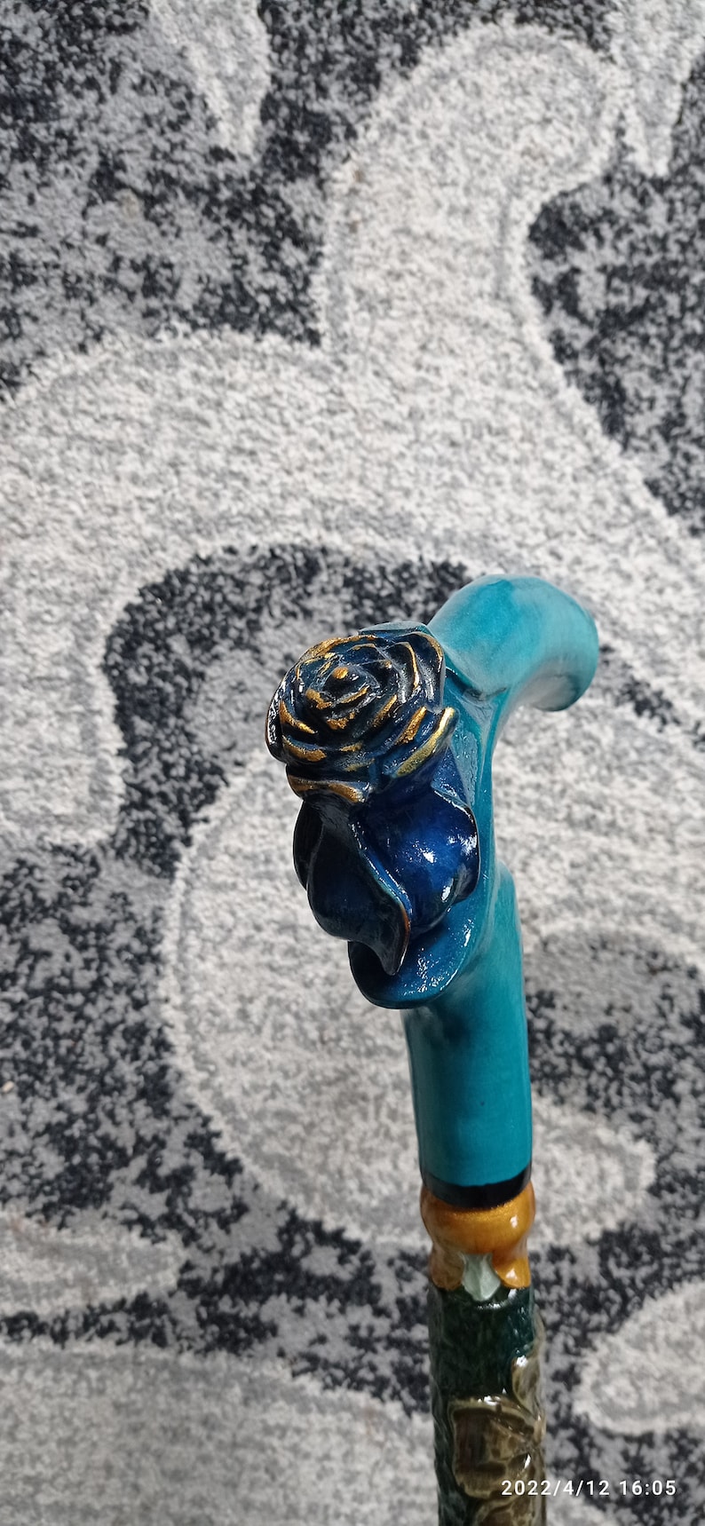 Puede incluir: Un bast&oacute;n de caminar azul turquesa con un dise&ntilde;o de rosa tallada. La rosa est&aacute; pintada de azul con detalles dorados.