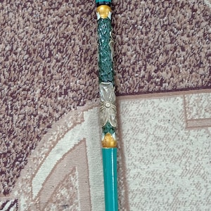 Puede incluir: Un bast&oacute;n de caminar verde azulado con un dise&ntilde;o floral tallado y una flor azul en la parte superior. El bast&oacute;n tiene una punta de goma negra.