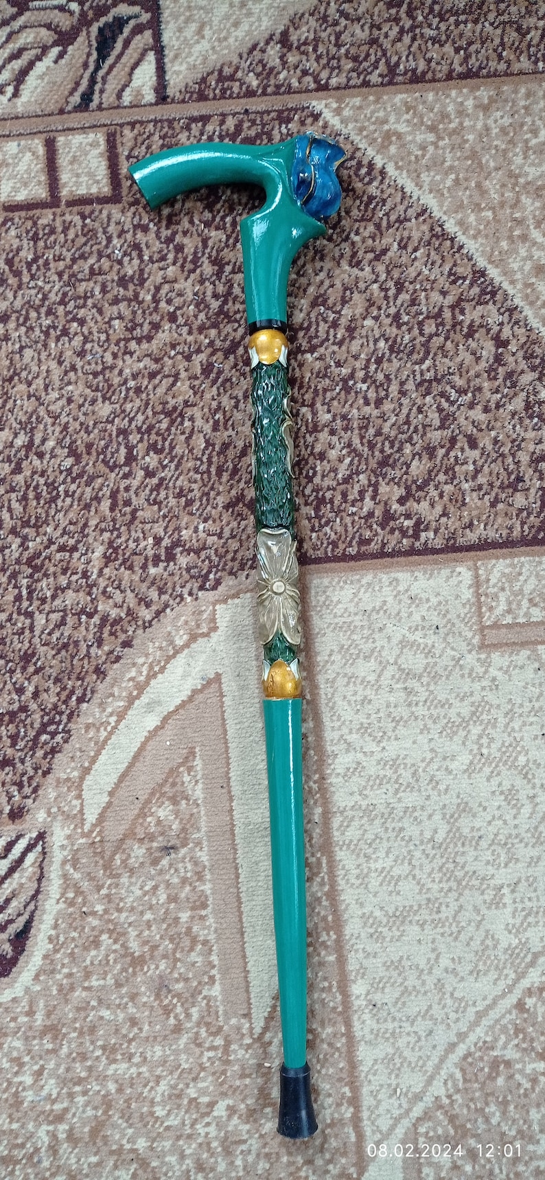 Puede incluir: Un bast&oacute;n de caminar verde azulado con un dise&ntilde;o floral tallado y una flor azul en la parte superior. El bast&oacute;n tiene una punta de goma negra.