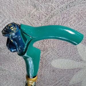 Puede incluir: Un bast&oacute;n de madera con un mango verde y una rosa azul tallada en la parte superior. El mango est&aacute; pintado con detalles dorados.