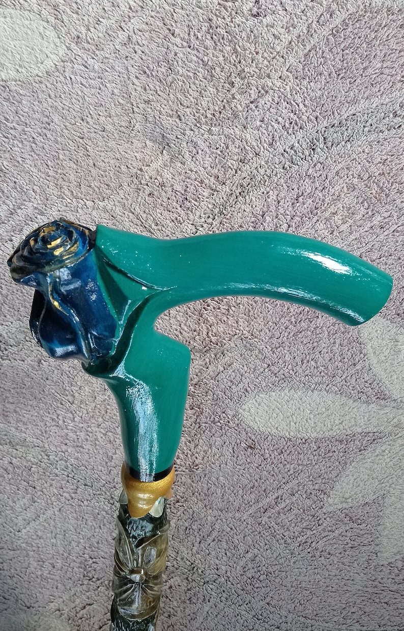 Puede incluir: Un bast&oacute;n de madera con un mango verde y una rosa azul tallada en la parte superior. El mango est&aacute; pintado con detalles dorados.