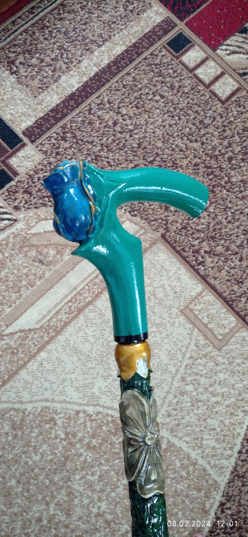 Puede incluir: Un bast&oacute;n de madera con un mango pintado de verde y azul. El mango est&aacute; tallado para parecer una rosa con detalles dorados. El bast&oacute;n est&aacute; decorado con una flor verde y blanca.