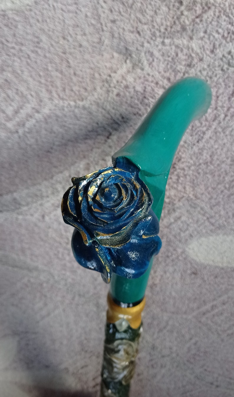 Puede incluir: Un bast&oacute;n de caminar azul turquesa con una rosa tallada azul y dorada en la parte superior.