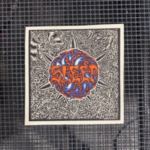 May include: Square patch with a black and white patterned border. The center features a blue and orange design with the word "SLEEP" in orange lettering. The background is a black mesh.