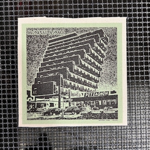 Peut inclure: Pièce d'art carrée en tissu avec une illustration en noir et blanc d'un immeuble à plusieurs étages et de voitures. Le texte "МОЛАТ ДОМА" est en haut, et un autre texte est en bas. Bordure vert clair.